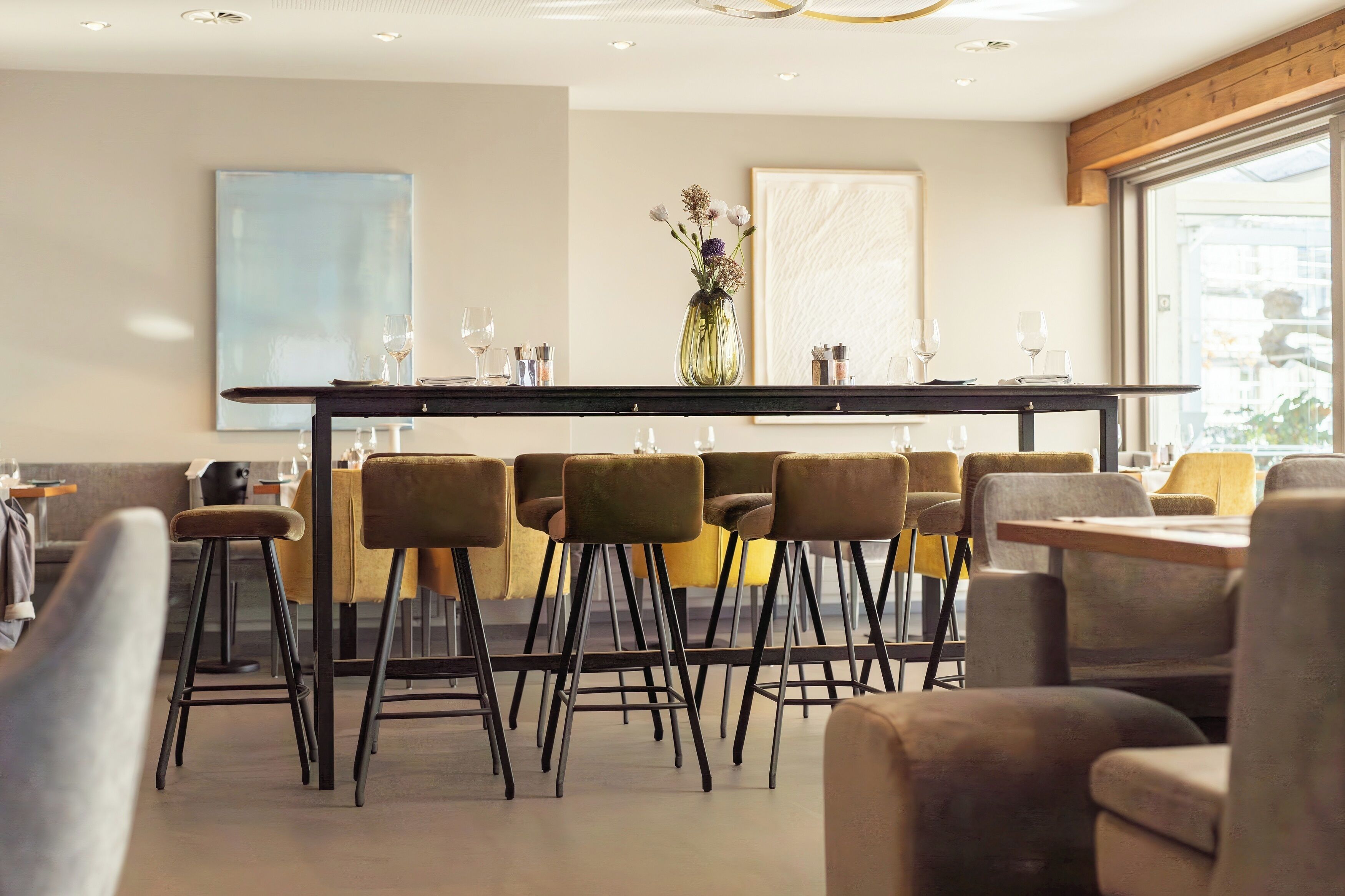 Un área de bar moderna con una barra larga, varios taburetes y un jarrón con flores.