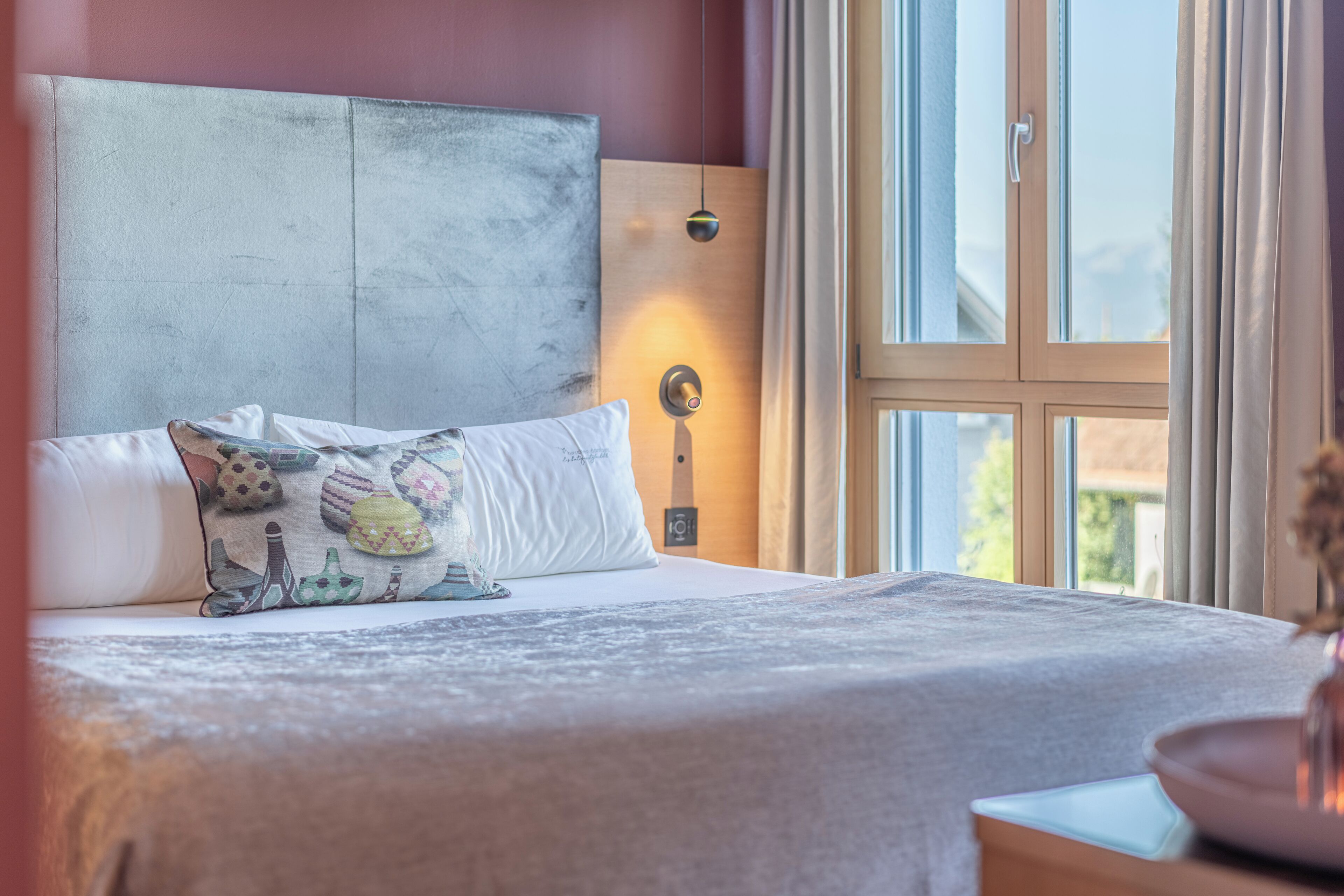 Une chambre à coucher avec un grand lit, une tête de lit, une table de chevet avec une lampe et une fenêtre avec des rideaux.