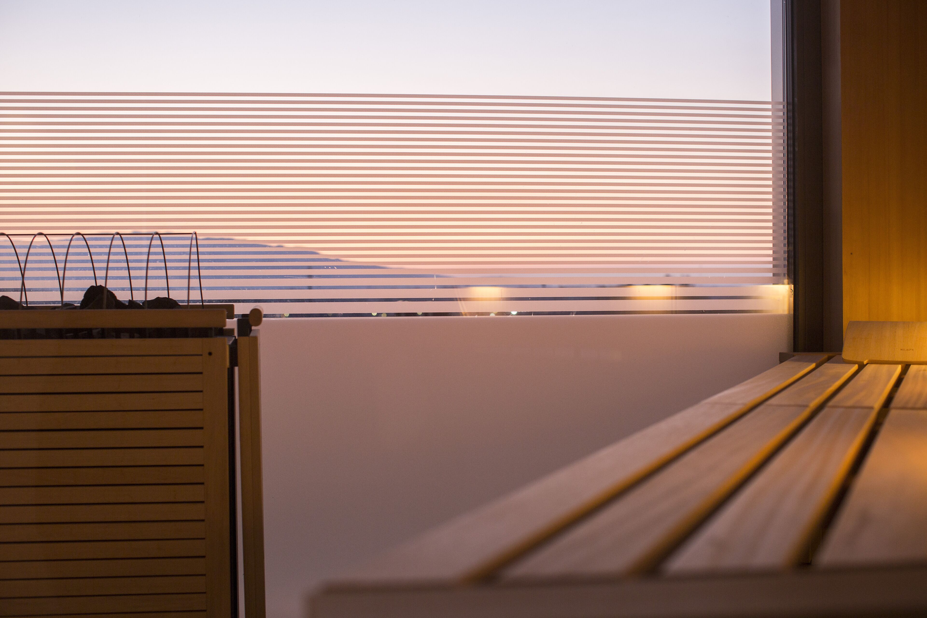 A view from a window with horizontal blinds, a wooden bench, and a radiator.