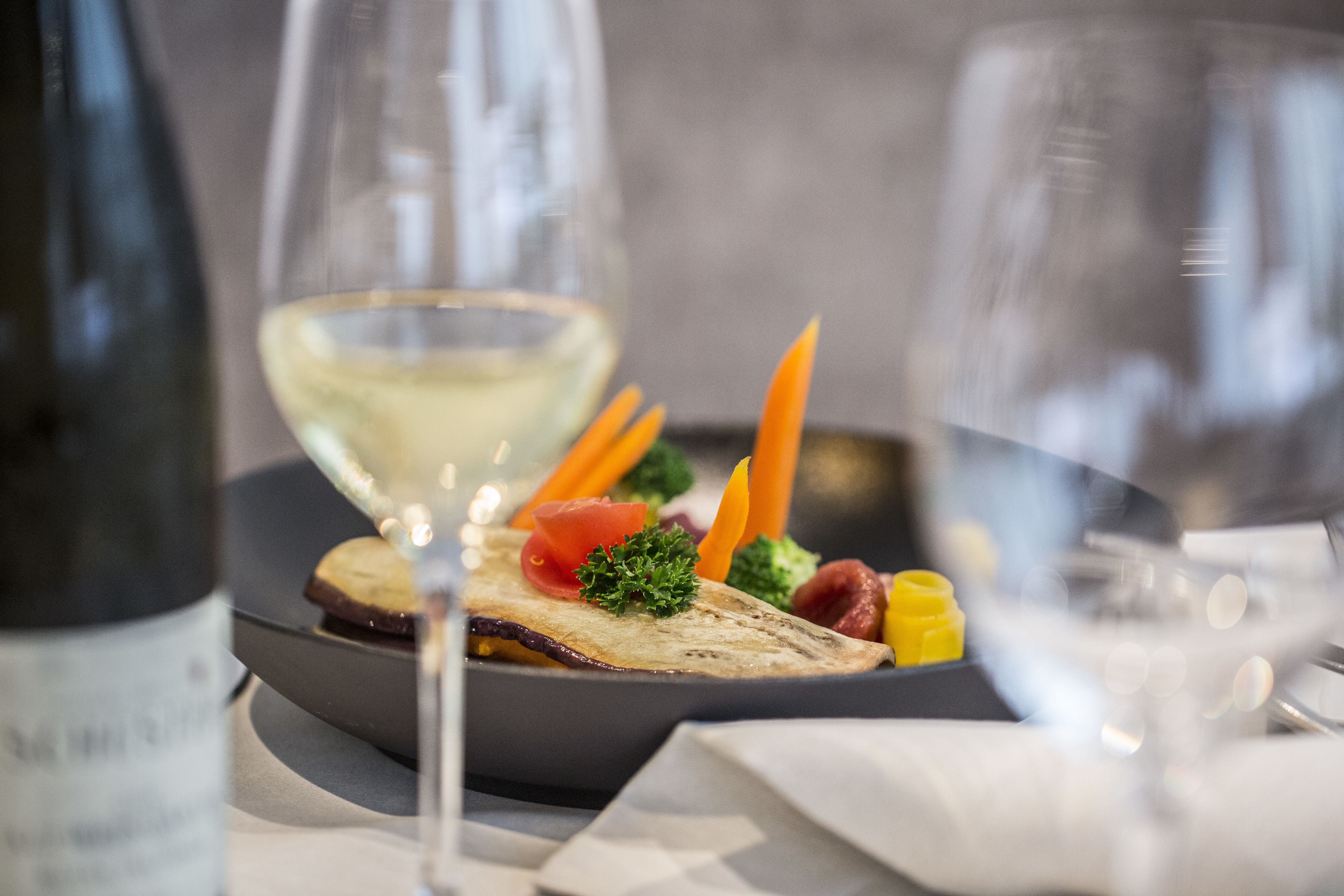 Una mesa de comedor con un plato de comida, una botella de vino y dos copas.
