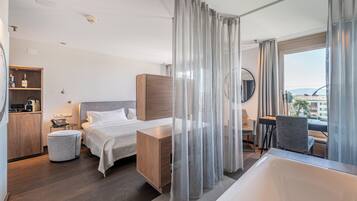Una habitación de hotel moderna con una cama grande, un escritorio, una silla, un espejo redondo y vistas a la ciudad a través de la ventana.
