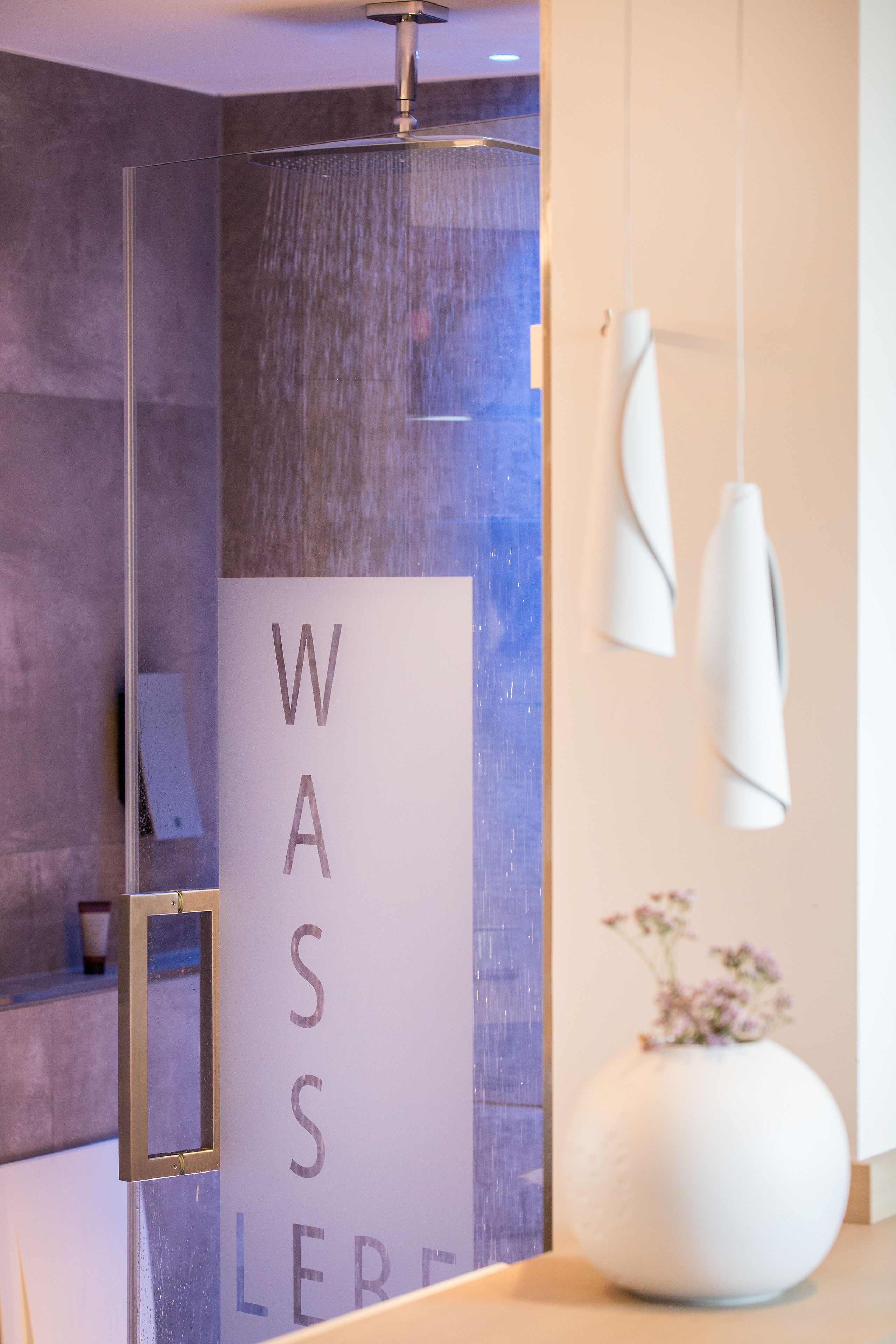 A modern bathroom with a glass shower enclosure, a white vase with flowers on the counter, and a towel rack.