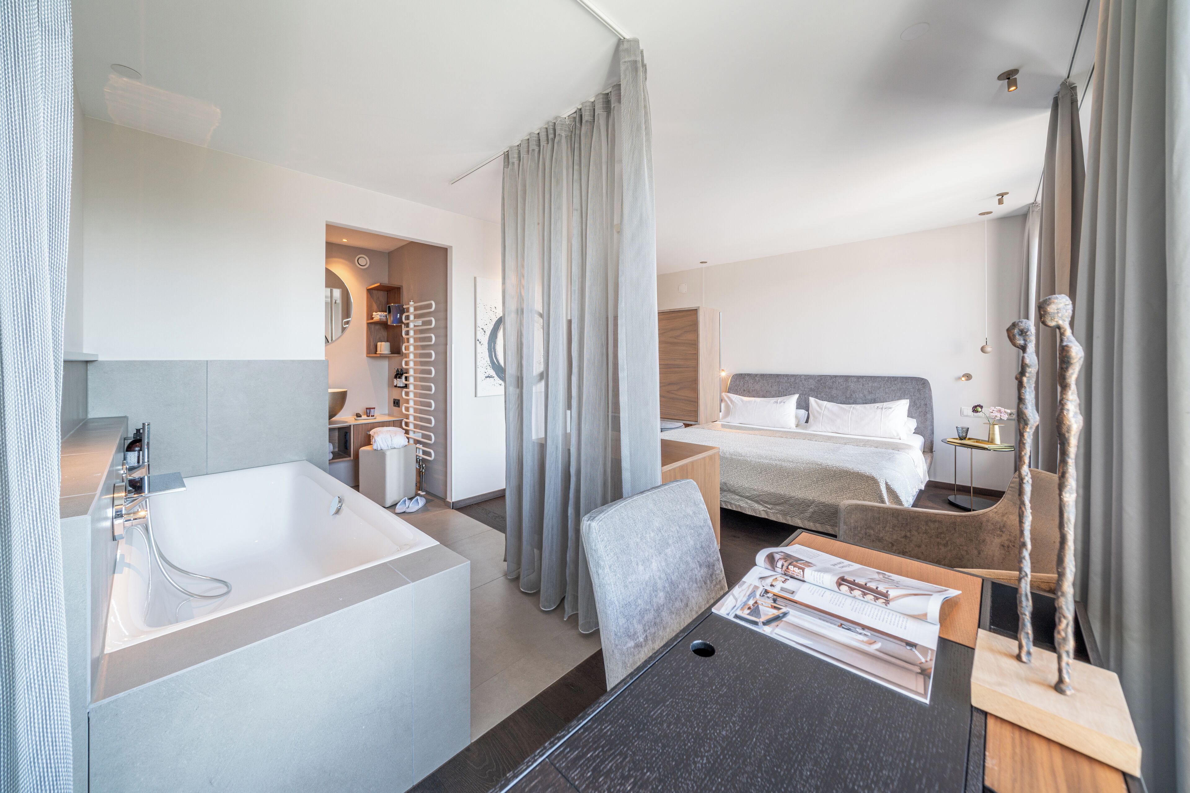 Une chambre d’hôtel moderne dotée d’une grande baignoire, d’une chambre à coucher séparée avec un lit, et d’un coin repas avec une table et des chaises.