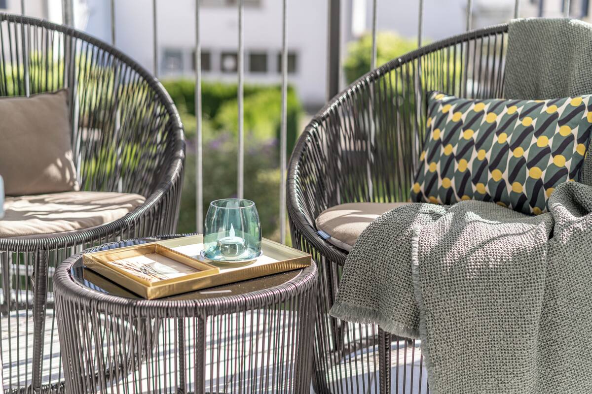 A wicker chair with a cushion and a tray with a glass and a book.