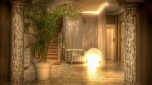 Un pasillo con columnas, una palma en maceta, una silla y un objeto esférico iluminado.