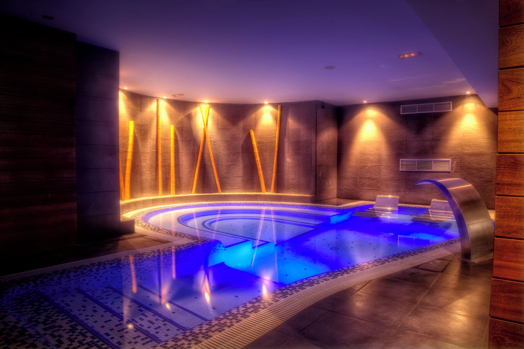 Un spa moderno con un jacuzzi circular, paredes de madera e iluminación ambiental.