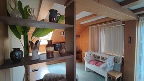 A cozy room with a white bed, a small table, and shelves with decorative items. - Pension & Café Sonnenkanzel (Sinntal)