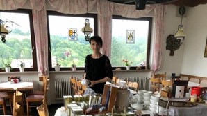 Una habitación con una mesa preparada para el té, una ventana con vistas y una persona de pie junto a la ventana.