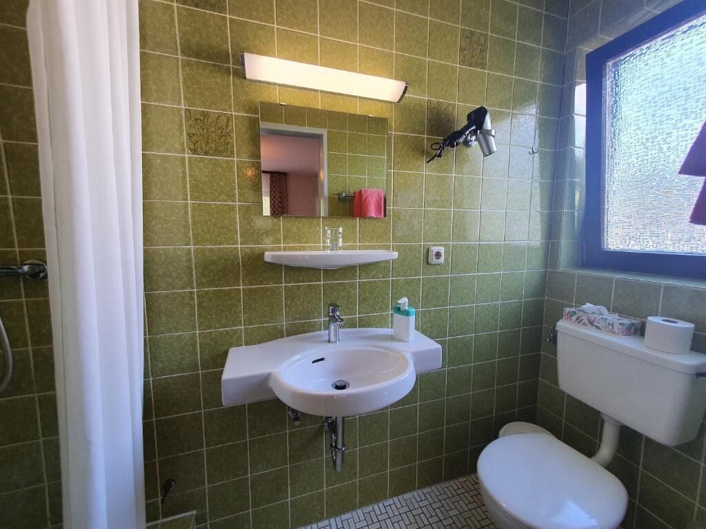 Un baño con lavamanos, espejo e inodoro blancos.