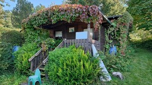 A wooden cabin with a porch, surrounded by lush greenery and a small staircase leading up to the entrance. - Pension & Café Sonnenkanzel (Sinntal)