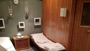 Una habitación con una silla de masaje, una mesita de madera con una tetera, una cama y un armario de madera.
