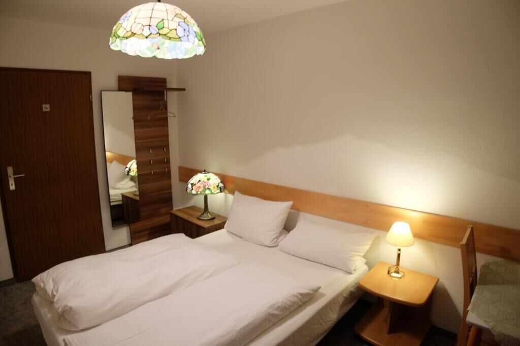 A hotel room with a bed, a nightstand with a lamp, a mirror, and a wooden headboard.