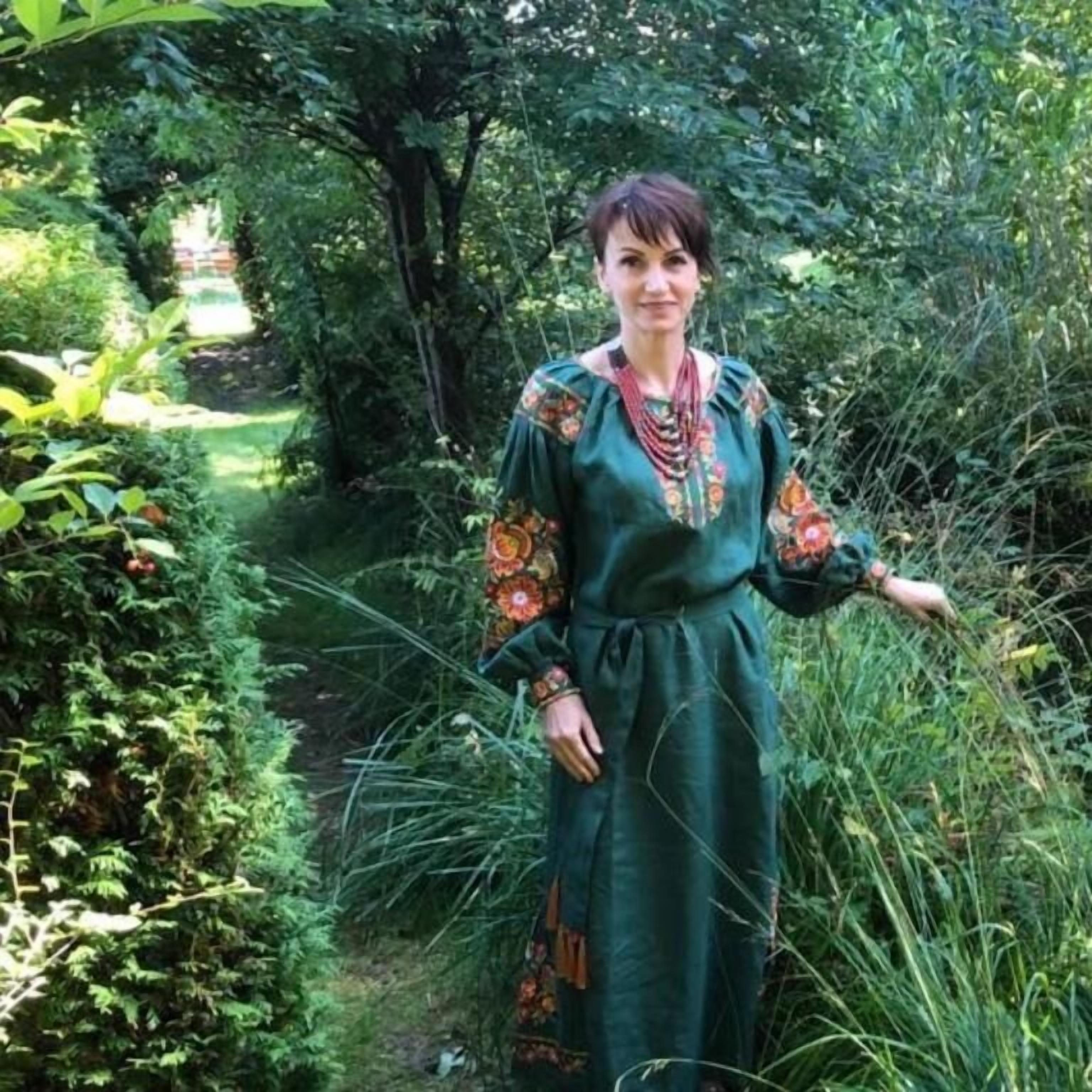 Une personne se tient dans un jardin où le feuillage est dense et où l’on aperçoit un sentier.