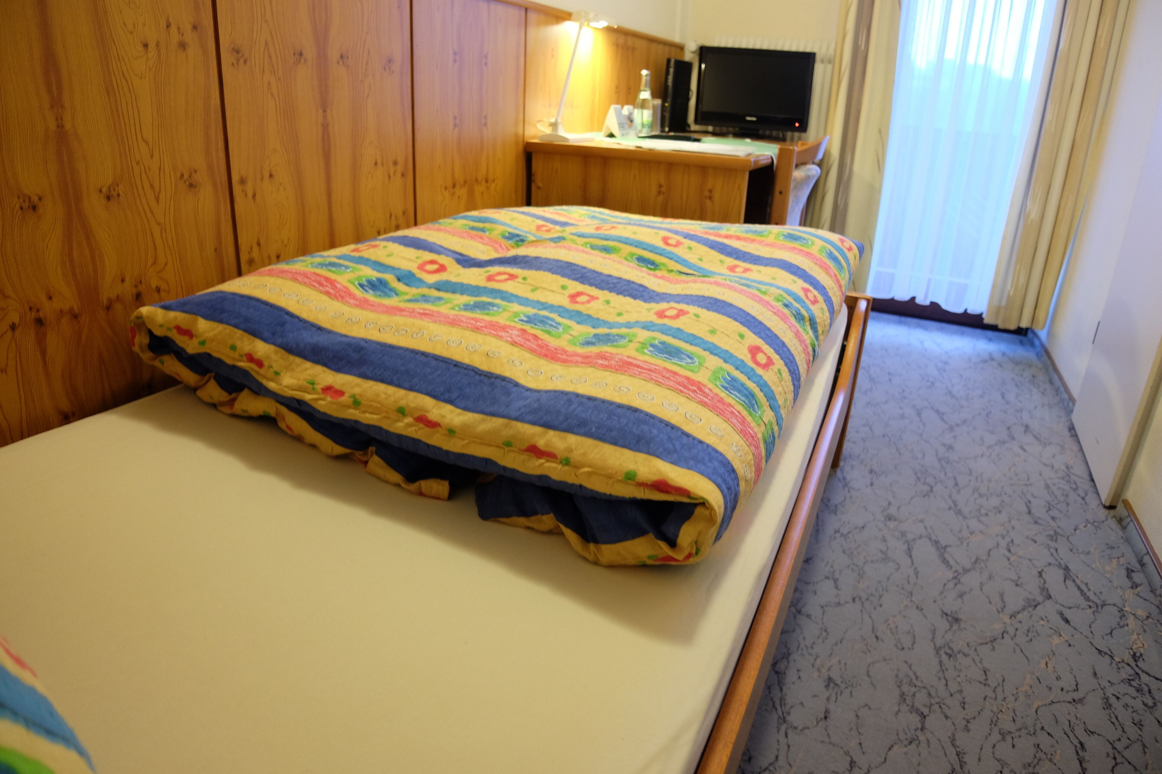 A bedroom with a bed, wooden wardrobe, desk, and a television.