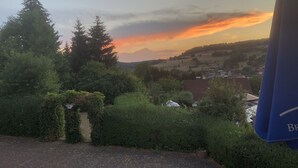 Vista de un paisaje rural con árboles, un camino pavimentado y un pueblo a lo lejos durante el atardecer.