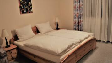 Un dormitorio con cama de madera, dos mesitas de noche, una lámpara, un cuadro en la pared y una ventana con cortinas.