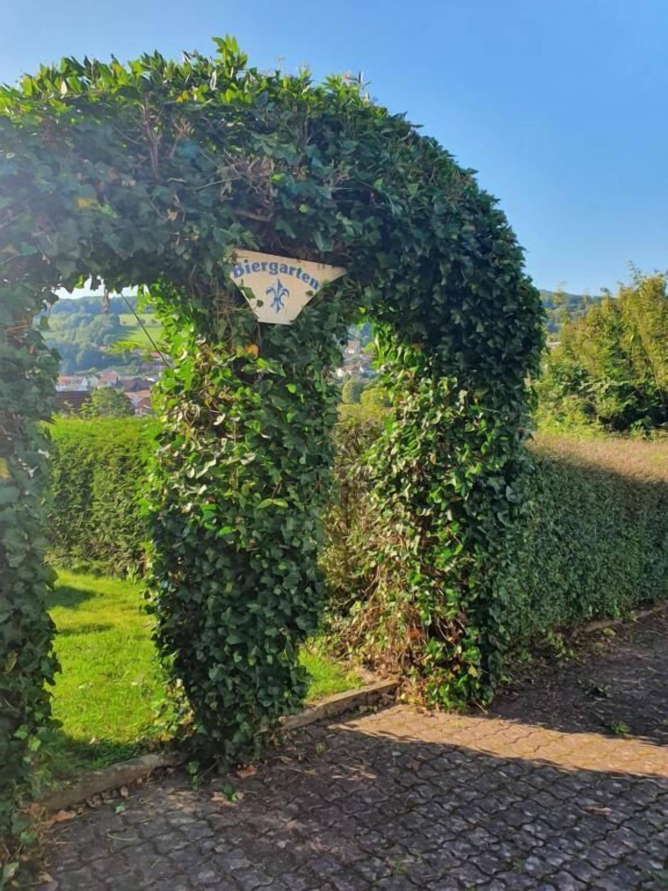 Ein Gartenweg mit einem Schild, auf dem 'Biergarten' steht, umgeben von üppigem Grün.