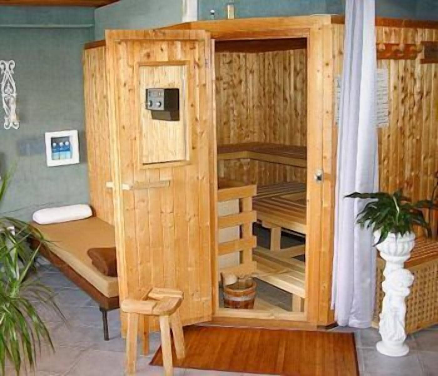 A wooden sauna with a bench and a small table, a wooden bench, and a potted plant.