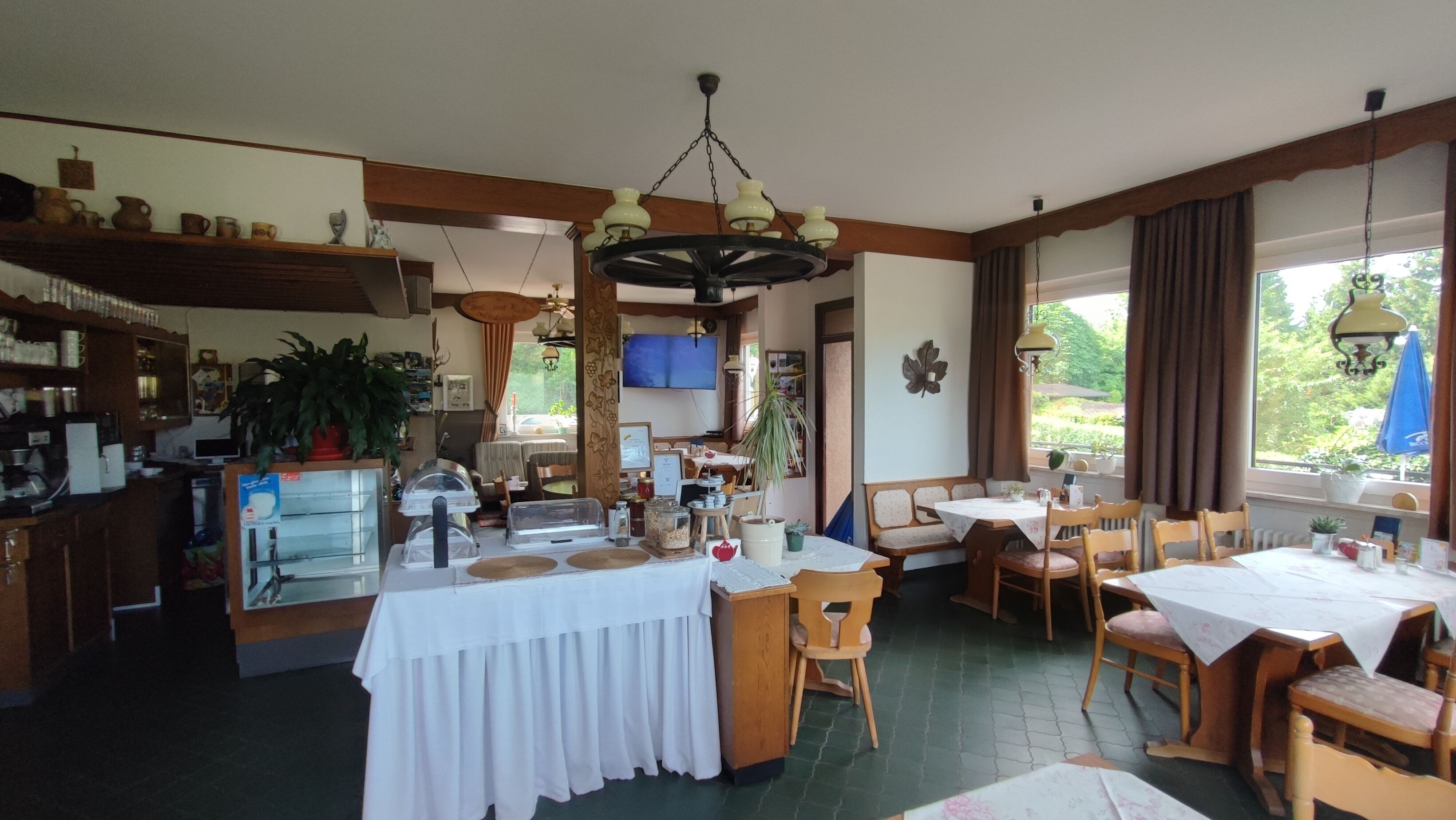 A restaurant with a central dining area, a bar area with shelves, and a television.