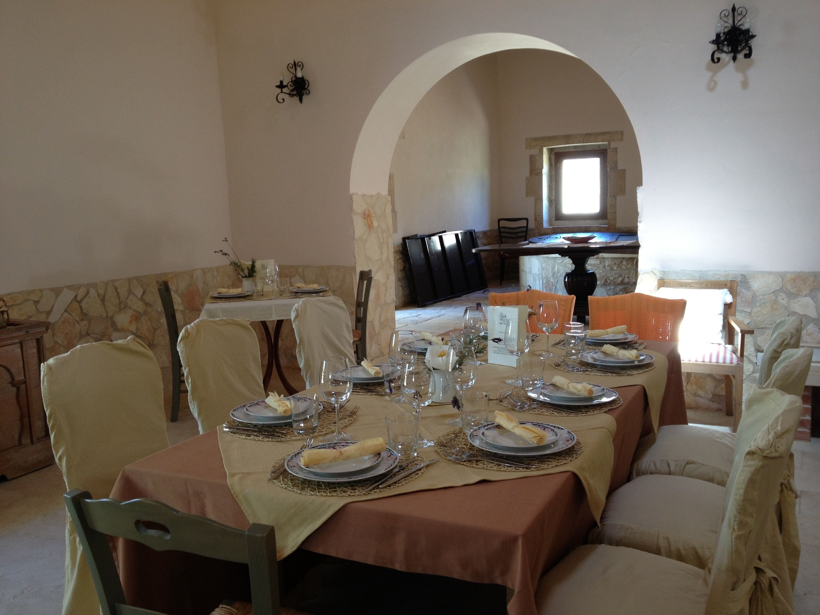 Comedor con una mesa dispuesta para seis personas, paredes de piedra y vistas a otra habitación a través de un arco.