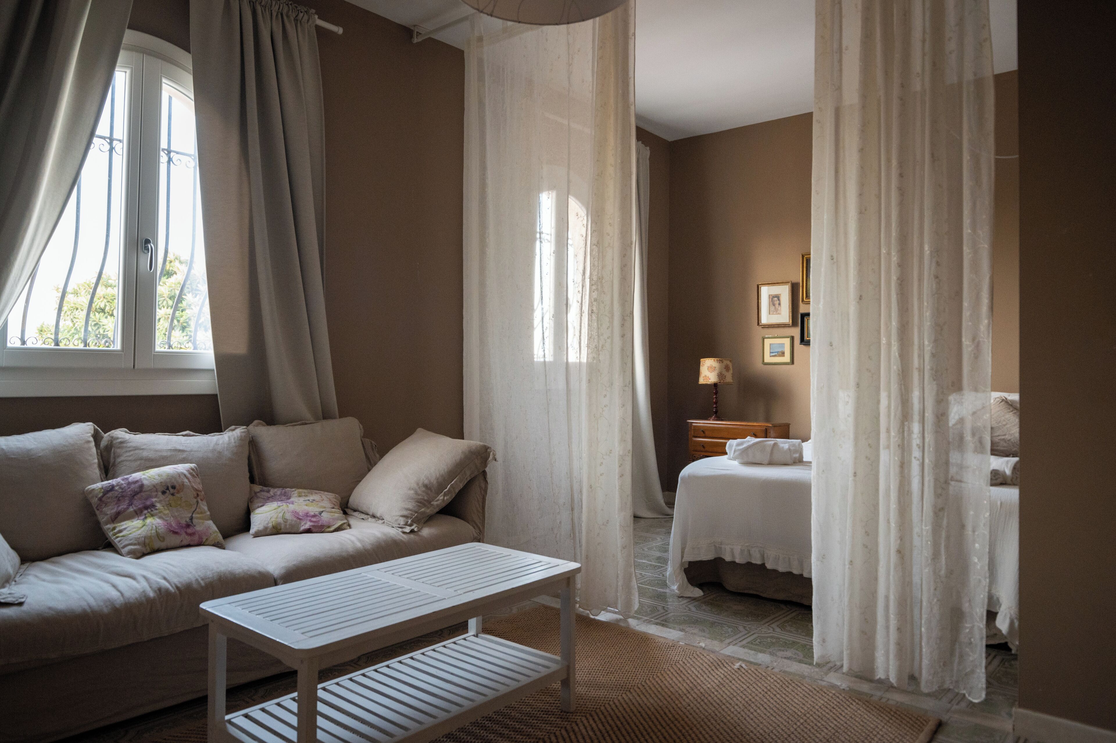 A bedroom with a bed, a bedside table, a nightstand, and a window with curtains.