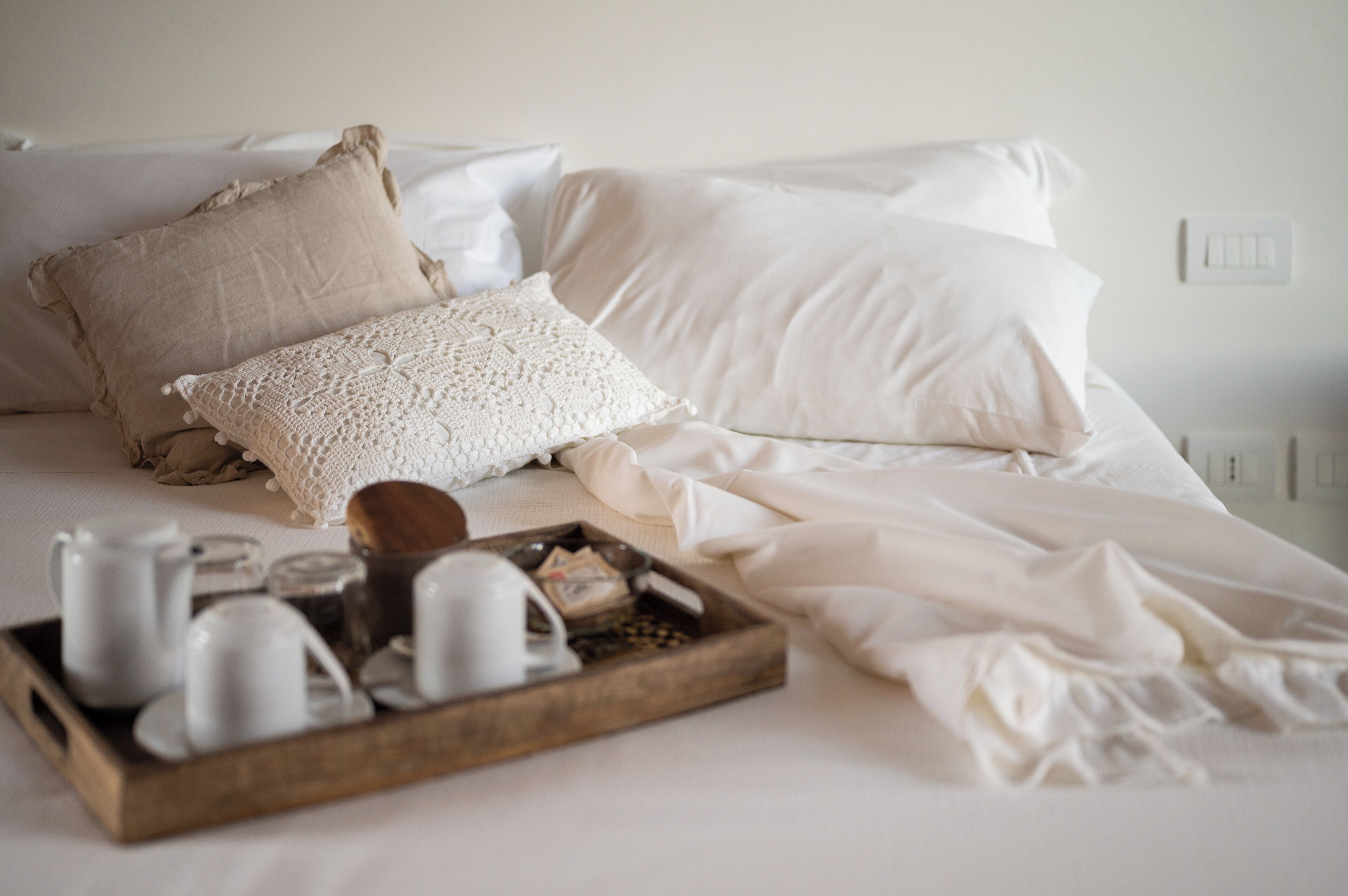 Una cama bien tendida con sábanas blancas y una bandeja de madera con tazas de té y una tetera.