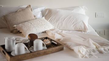 Una cama bien tendida con sábanas blancas y una bandeja de madera con tazas de té y una tetera.