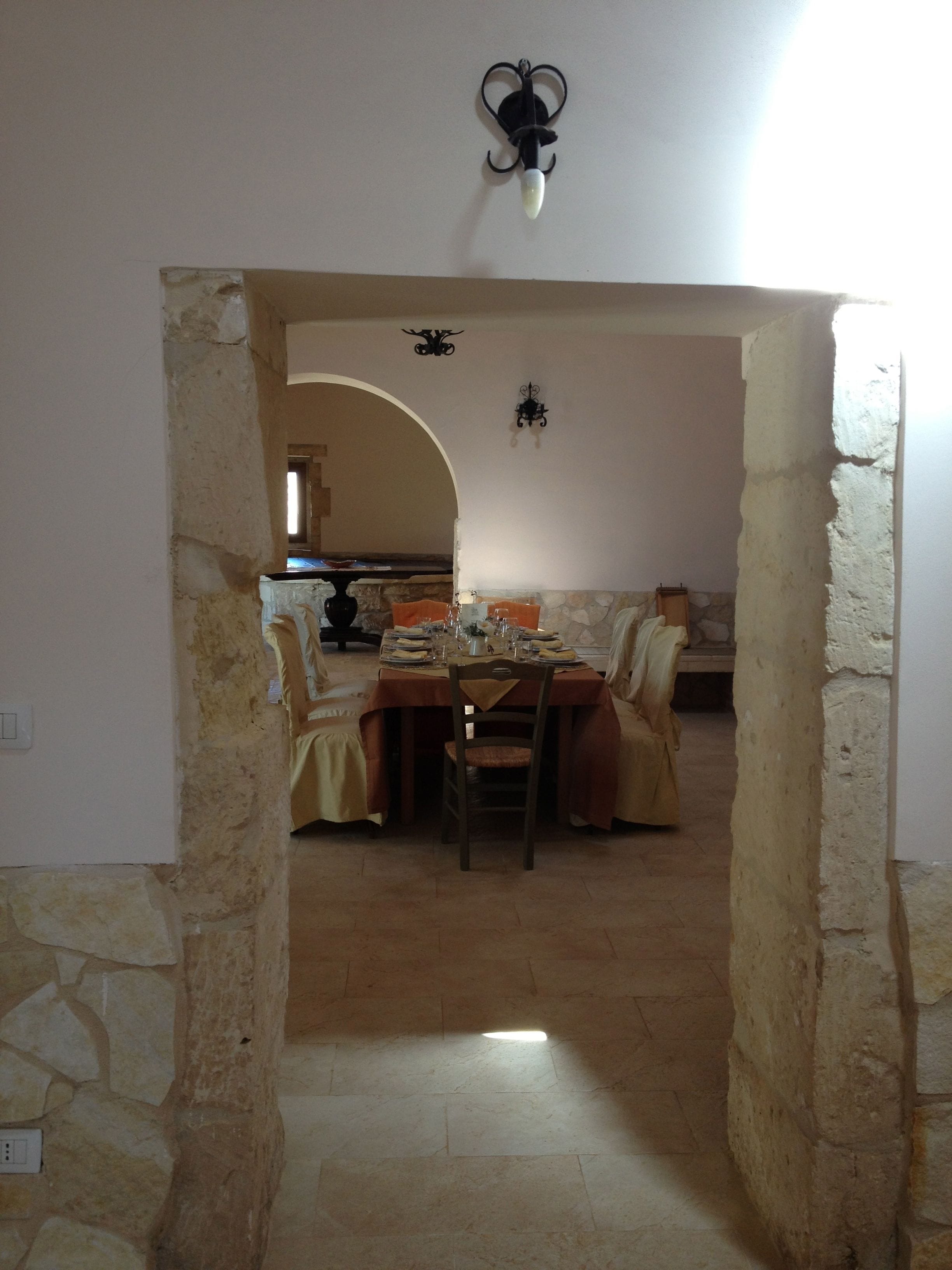 A dining area with a stone wall, a table set for two, and a chandelier.