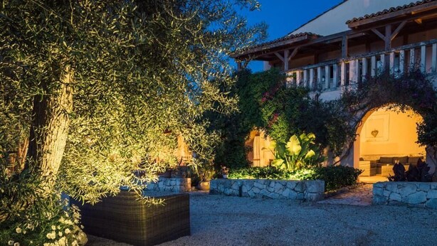 Une cour avec un grand arbre, des murs en pierre et un bâtiment doté d’un toit en tuiles.