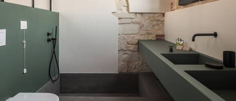A bathroom with a green wall, a white toilet, a stone accent wall, a bathtub, and a modern sink with a faucet.