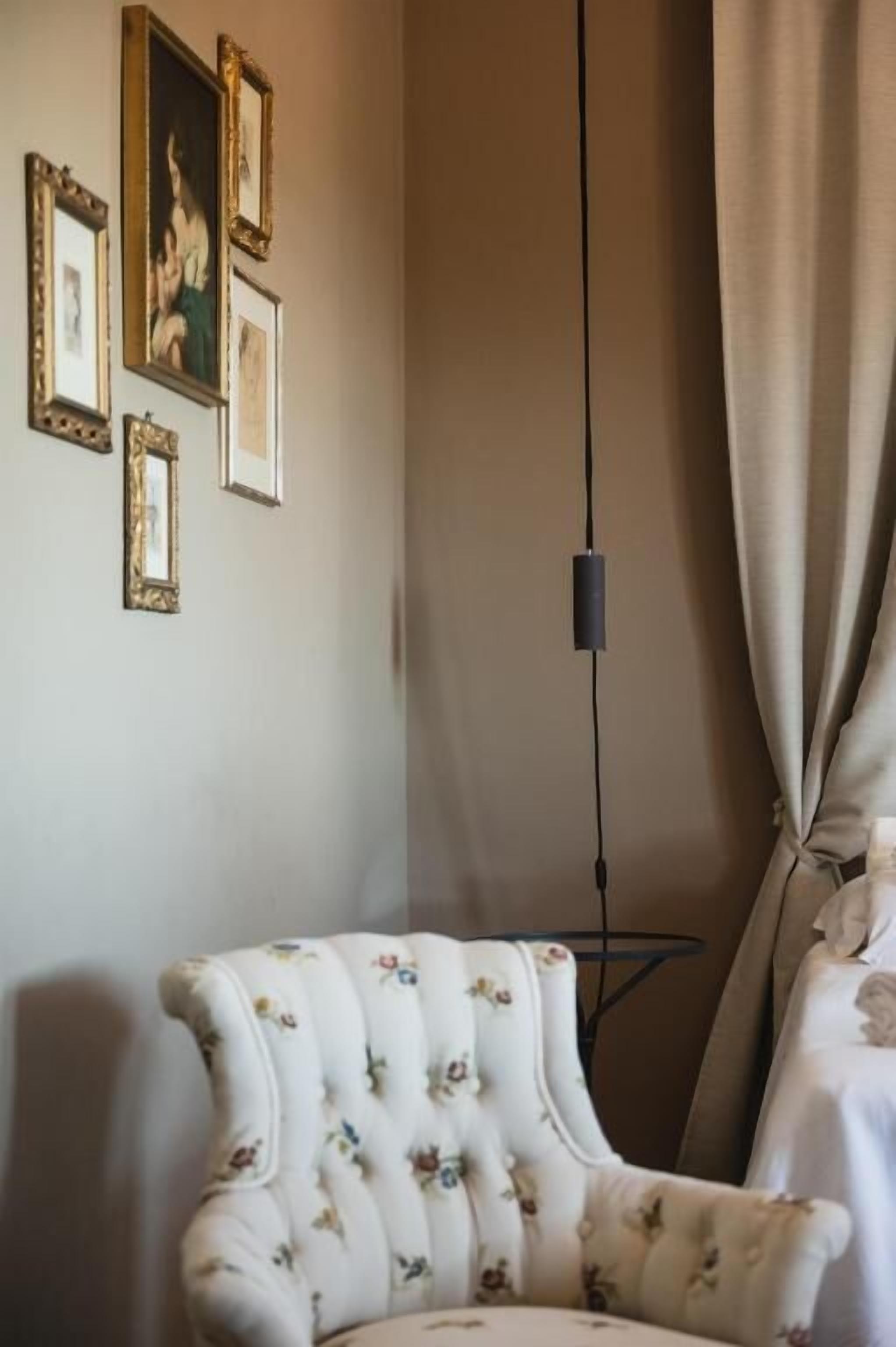 A room with a floral upholstered armchair, a wall-mounted picture frame, and a hanging light fixture.