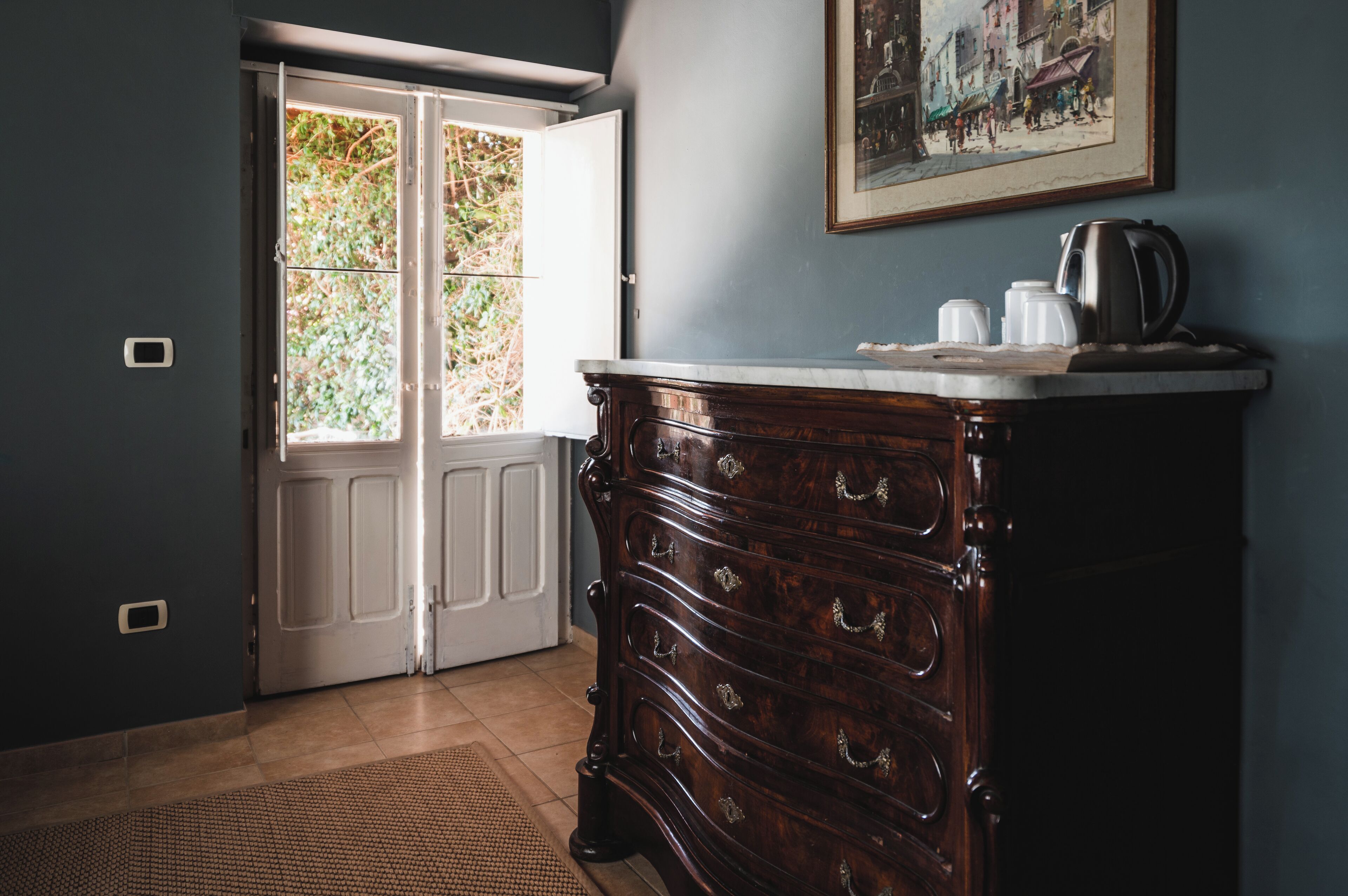 A room with a wooden dresser, a painting on the wall, and a door leading to a garden.