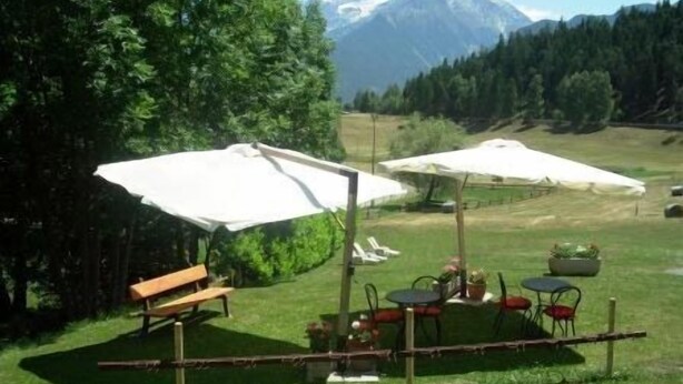 An outdoor seating area with tables and chairs under umbrellas, a wooden bench, and a view of a mountain range. - Saint Nicolas (Saint-Nicolas)