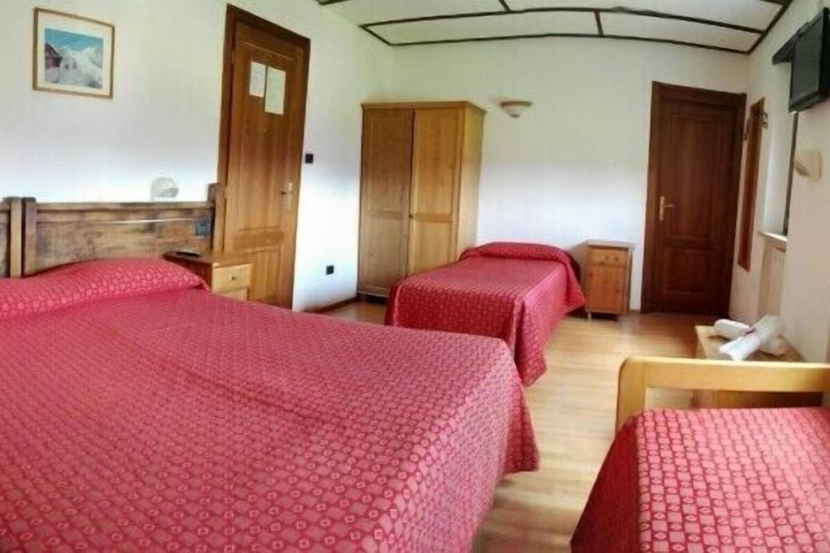 A hotel room with two beds, wooden headboards, a wooden wardrobe, and a small table.