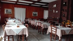 Uma sala de jantar com várias mesas e cadeiras, painéis de madeira nas paredes e quadros emoldurados.