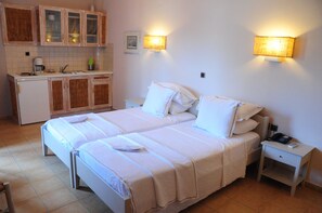 A hotel room with two beds, a small kitchenette, and bedside lamps. - Ammos Naxos (Naxos)