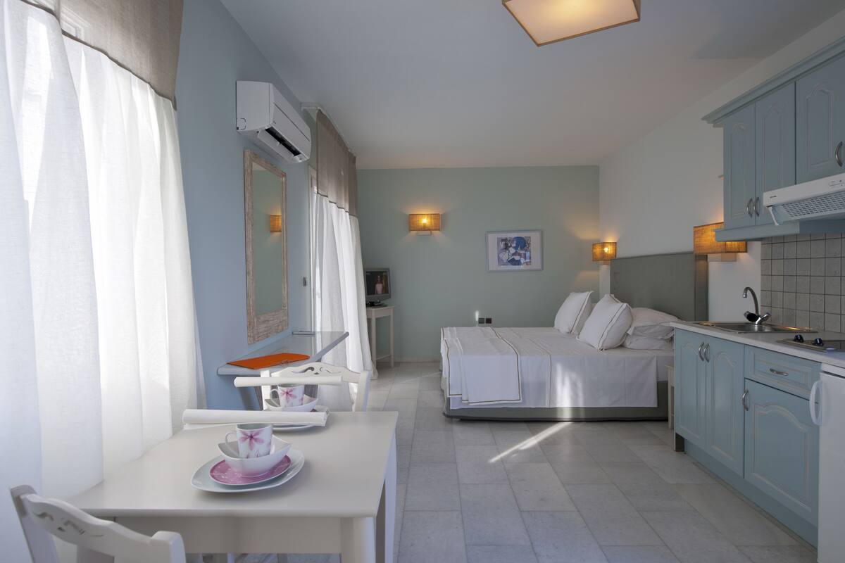 A compact hotel room with a bed, a small dining table, a kitchenette, and a bathroom.