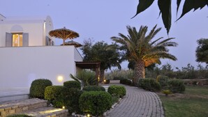 Un sendero que conduce a un edificio blanco con zona de estar al aire libre cubierta y palmeras.