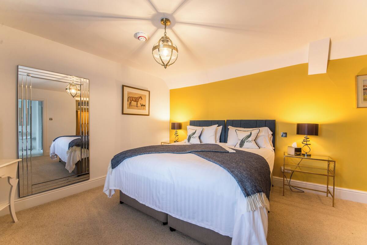 Een slaapkamer met een groot bed, een nachtkastje, een spiegel en een plafondventilator.