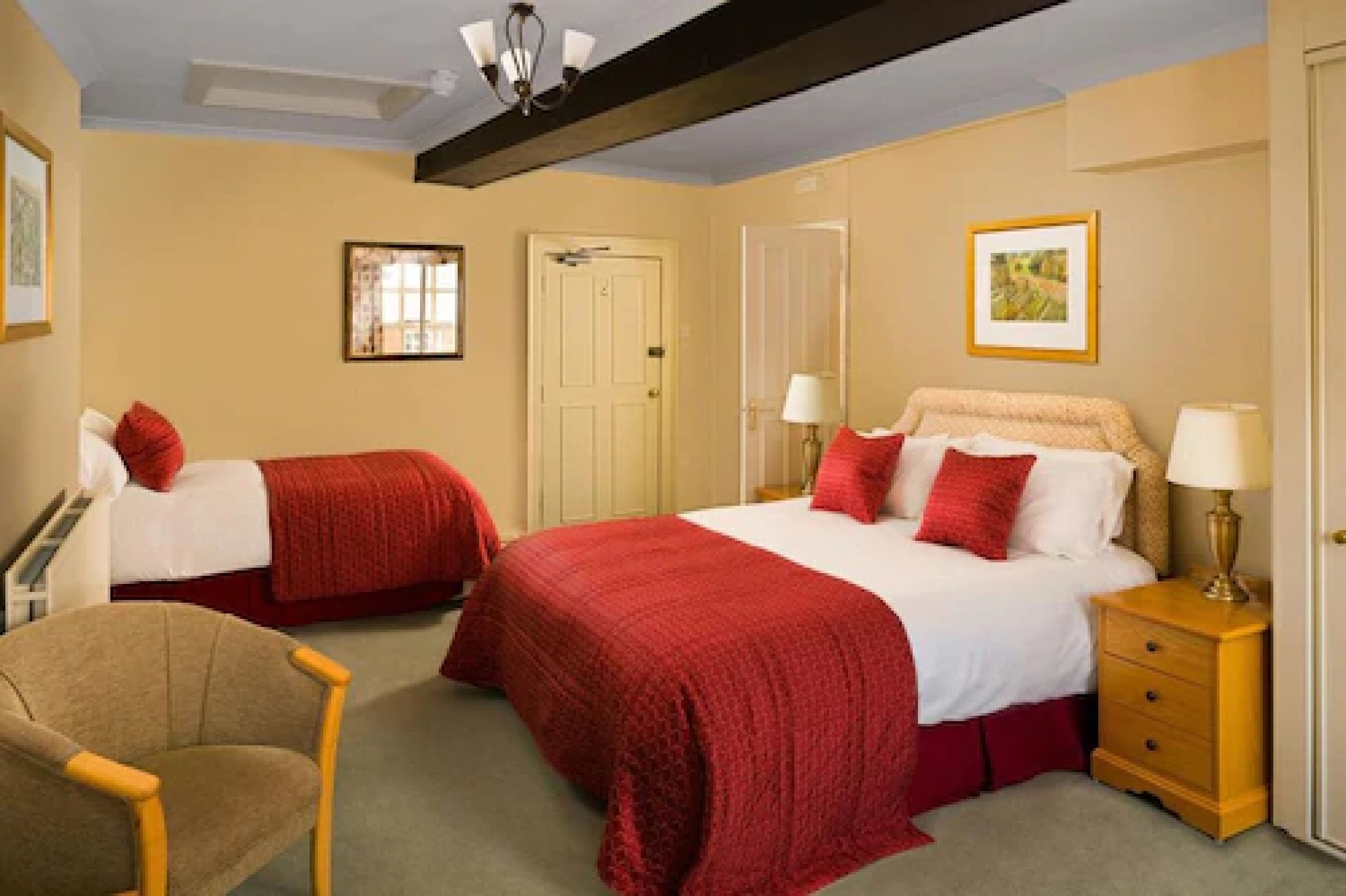 A hotel room with two beds, a chair, a nightstand, and a door.