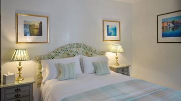Una cama bien hecha con un cabecero floral, dos mesitas de noche con lámparas y tres cuadros en las paredes.