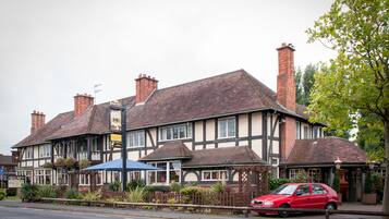 A traditional pub with a Tudor-style facade, a red car parked in front, and a blue umbrella providing shade.