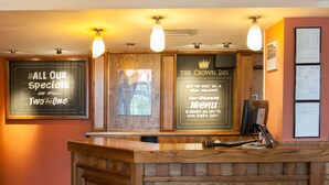 A hotel reception area with a wooden reception desk, framed welcome signs, and a menu board. - Crown, Droitwich by Marston's Inns (Droitwich)