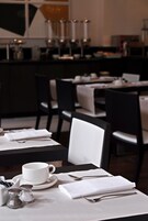 Un comedor con mesas dispuestas para dos, cada una con taza, platillo y cubiertos blancos.