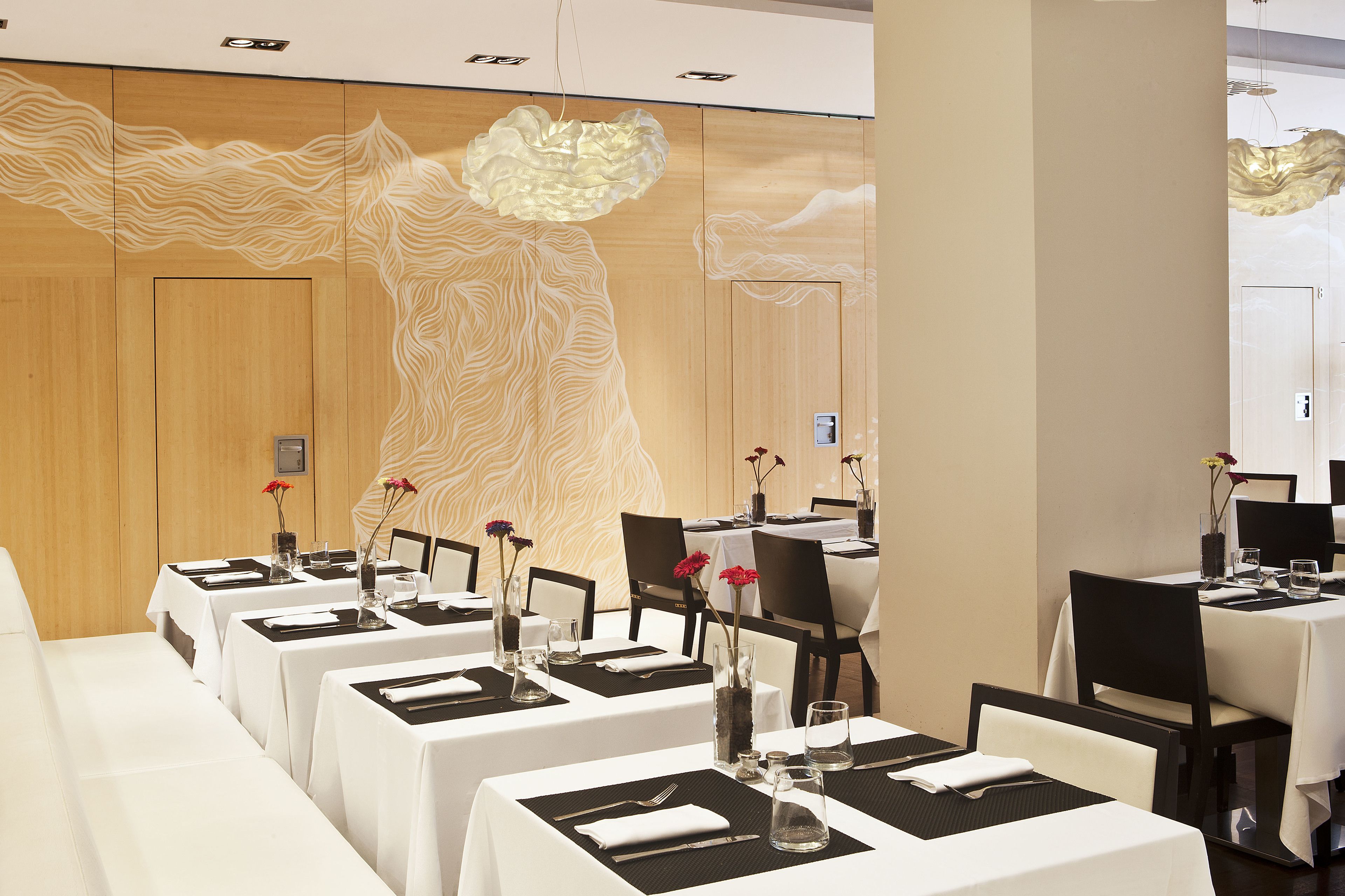 A dining area with tables set for service, featuring a modern design with wooden paneling and a unique light fixture.