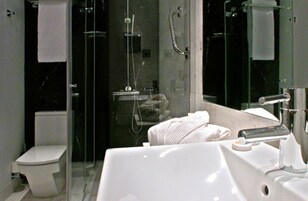 Uma casa de banho moderna com cabine de duche em vidro, sanita branca e lavatório com espelho.