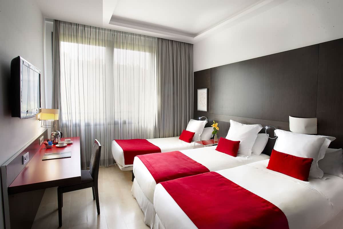A hotel room with two beds, a desk, a chair, a TV, and a window with curtains.