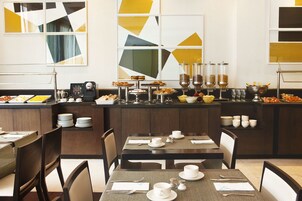 A buffet setup with various food items and beverages, neatly arranged tables with chairs, and a modern interior design with geometric wall art.