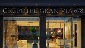 Exterior del Grupotel Gran Via 678 con diseño moderno, destacando amplios ventanales de vidrio y un espacio interior con mesas.