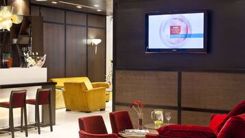 Un moderno vestíbulo de hotel con área de bar, asientos rojos y amarillos, y un televisor que muestra el canal BBC World News Business.